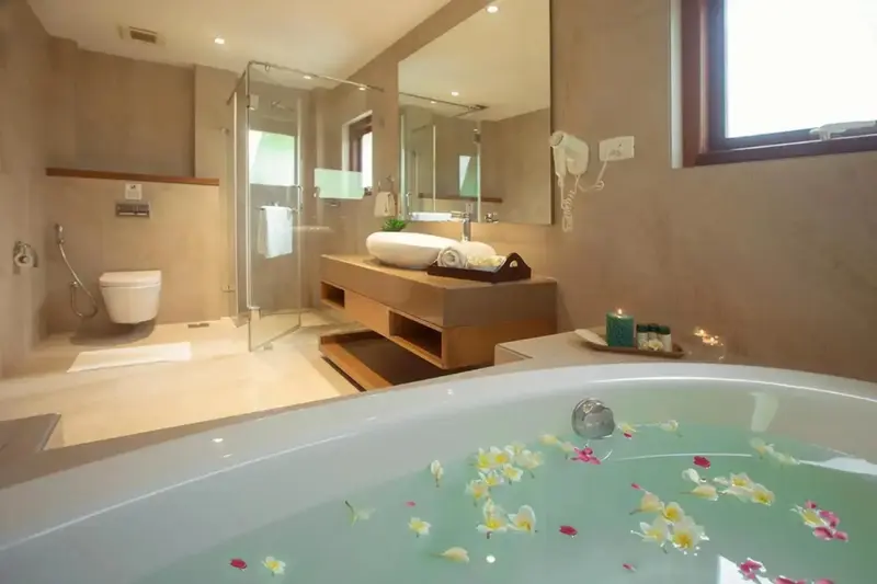 Une baignoire remplie d'eau est décorée de fleurs, dans une salle de bain lumineuse.