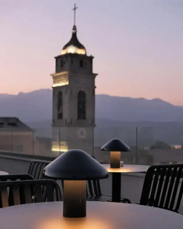 Tables et chaises sur une terrasse avec une tour illuminée en arrière-plan.