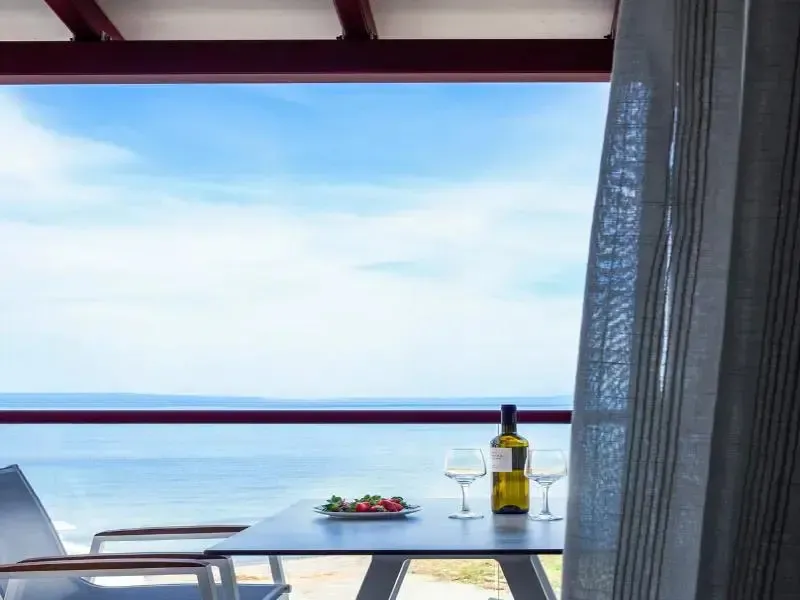 Une table avec une bouteille de vin et des fruits est placée devant une vue sur la mer.