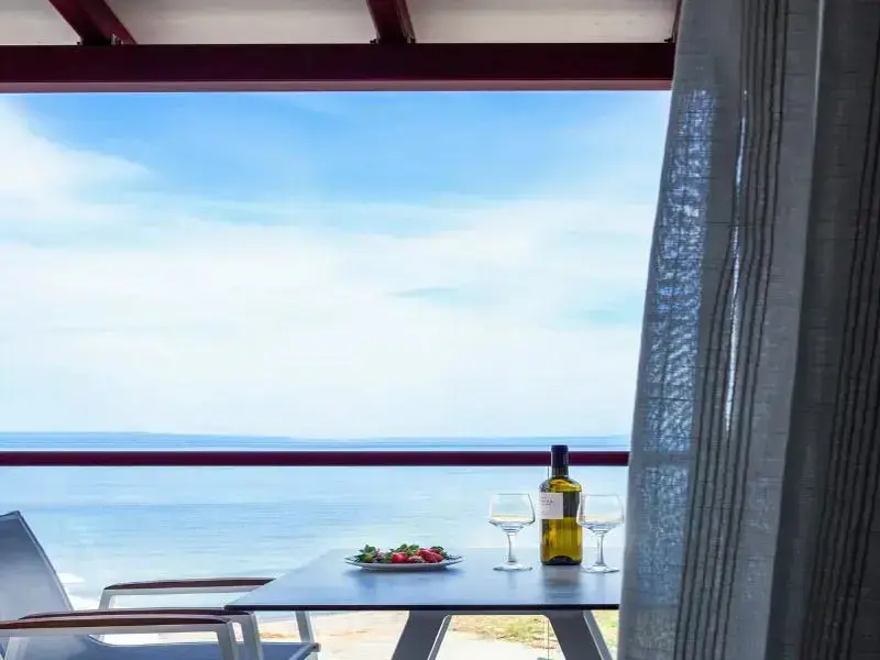 Une table avec une bouteille de vin et des fruits est placée devant une vue sur la mer.