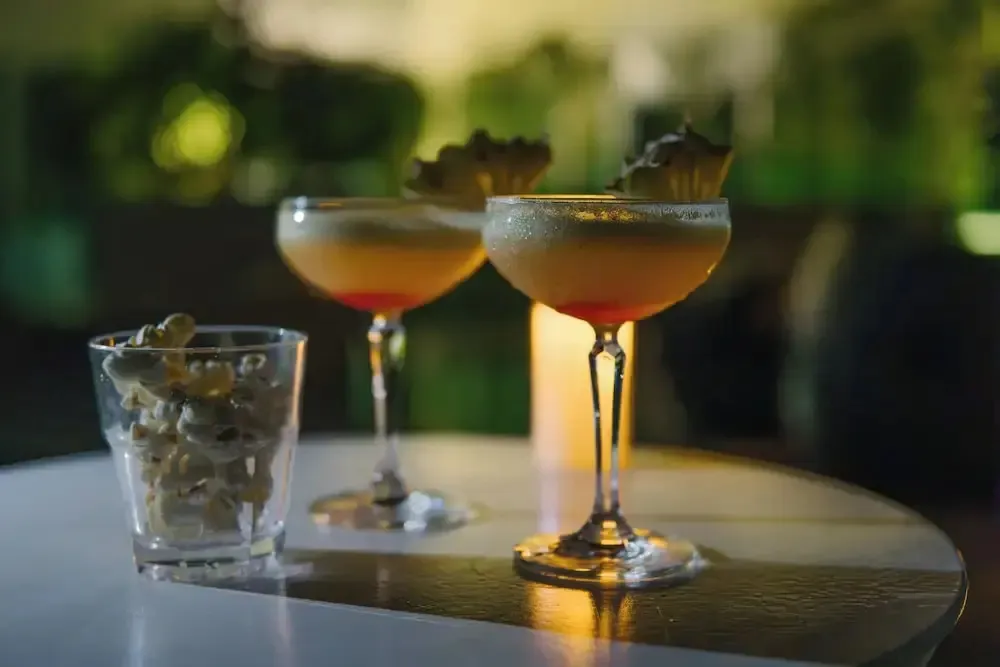 Deux cocktails colorés sont servis avec un accompagnement de popcorn sur une table ronde.