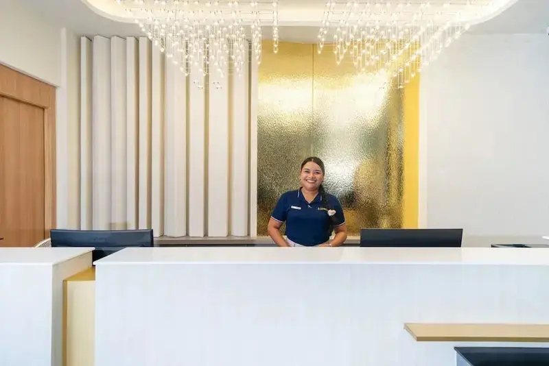Employée souriante derrière un comptoir d'accueil moderne et lumineux.