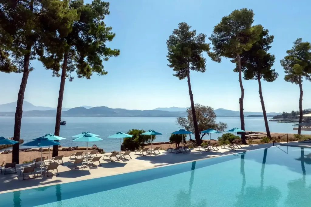 Une piscine bordée de transats et de parasols offre une vue sur la mer et les collines environnantes.