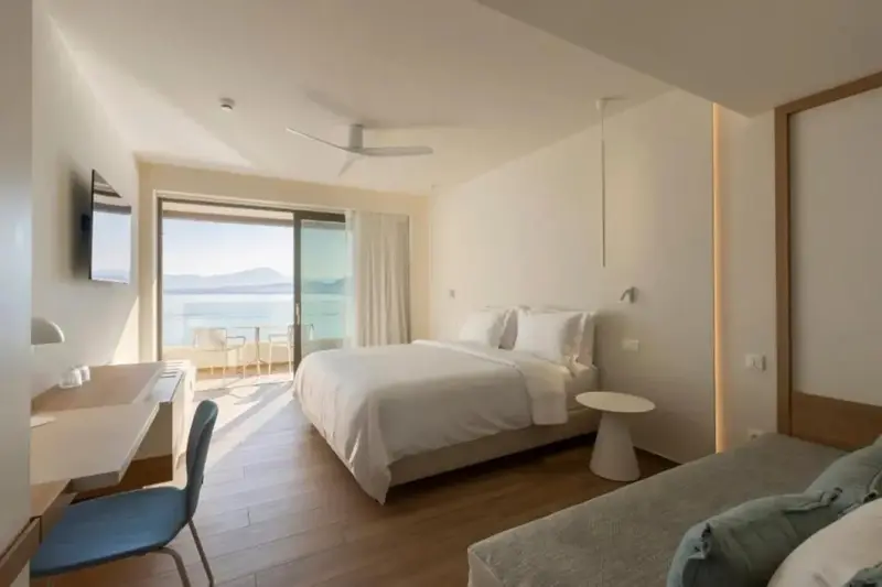 Une chambre lumineuse avec un grand lit et un accès à un balcon avec vue sur la mer.