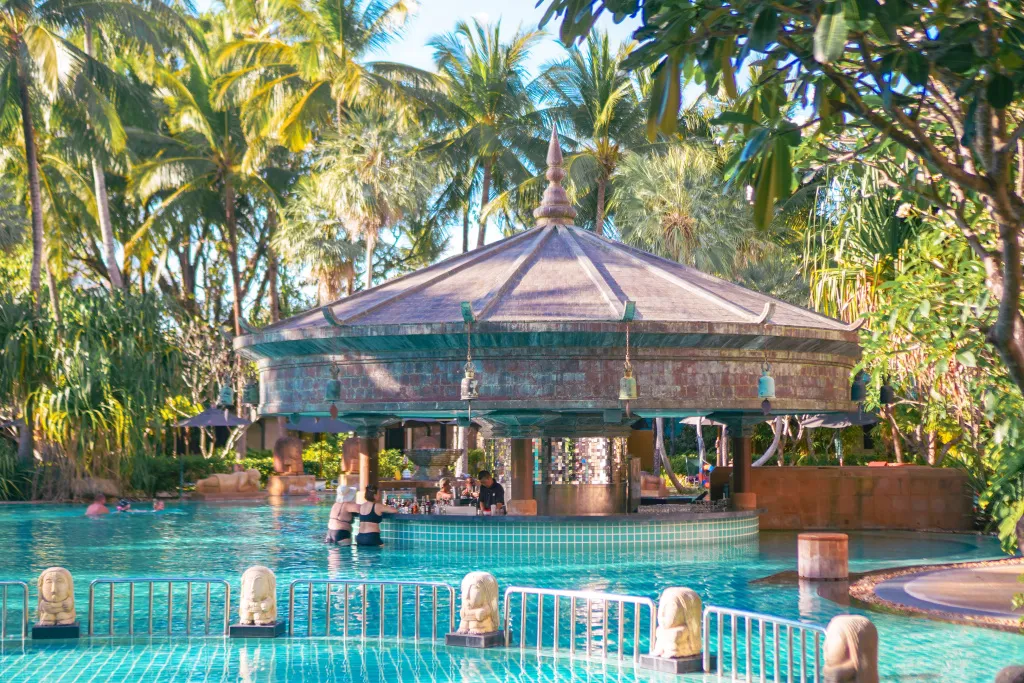 Un bar au centre d'une piscine turquoise, entouré de végétation luxuriante.