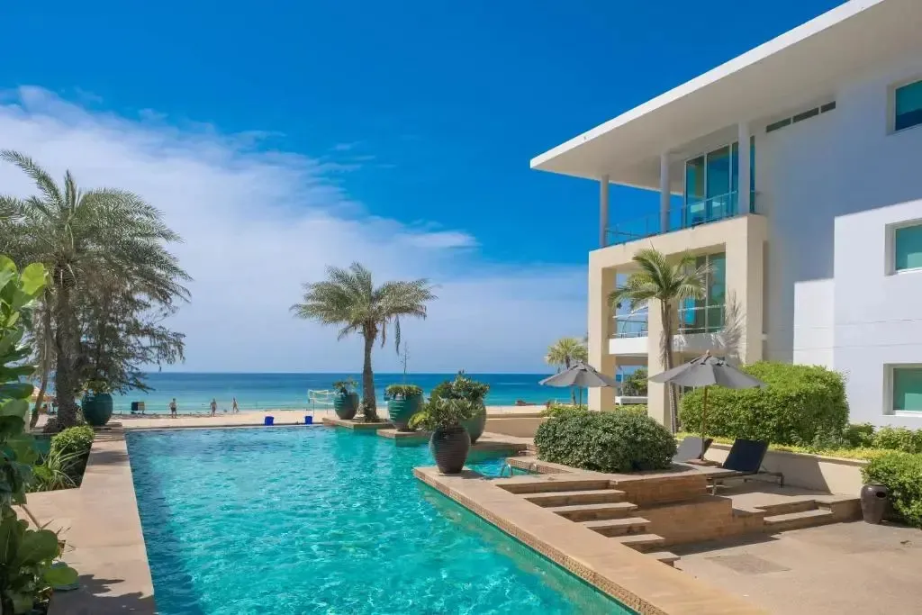 Une piscine turquoise bordée de palmiers et de transats, avec la mer en arrière-plan.