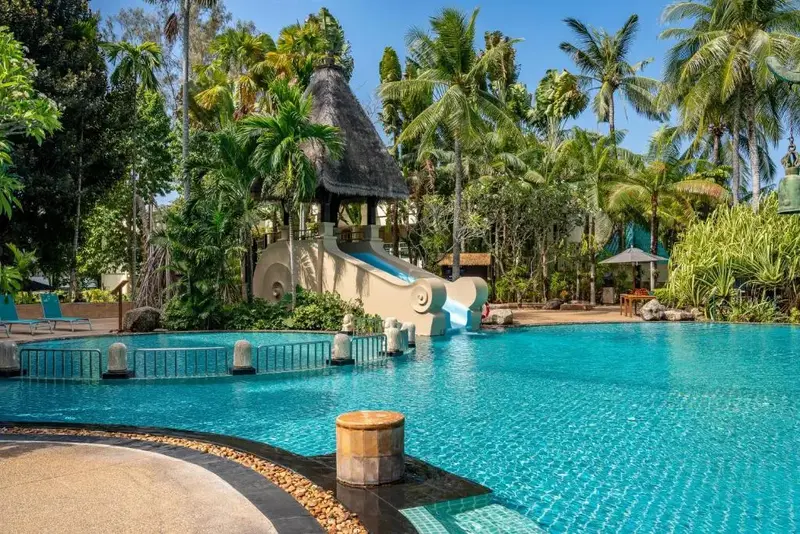Une grande piscine avec un toboggan aquatique et des palmiers.