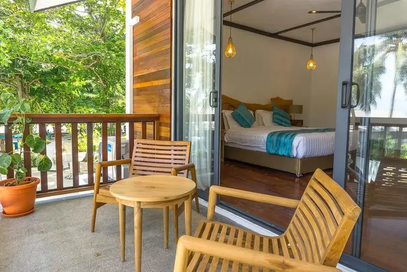 Une terrasse en bois donne sur une chambre lumineuse avec un lit décoré de coussins.