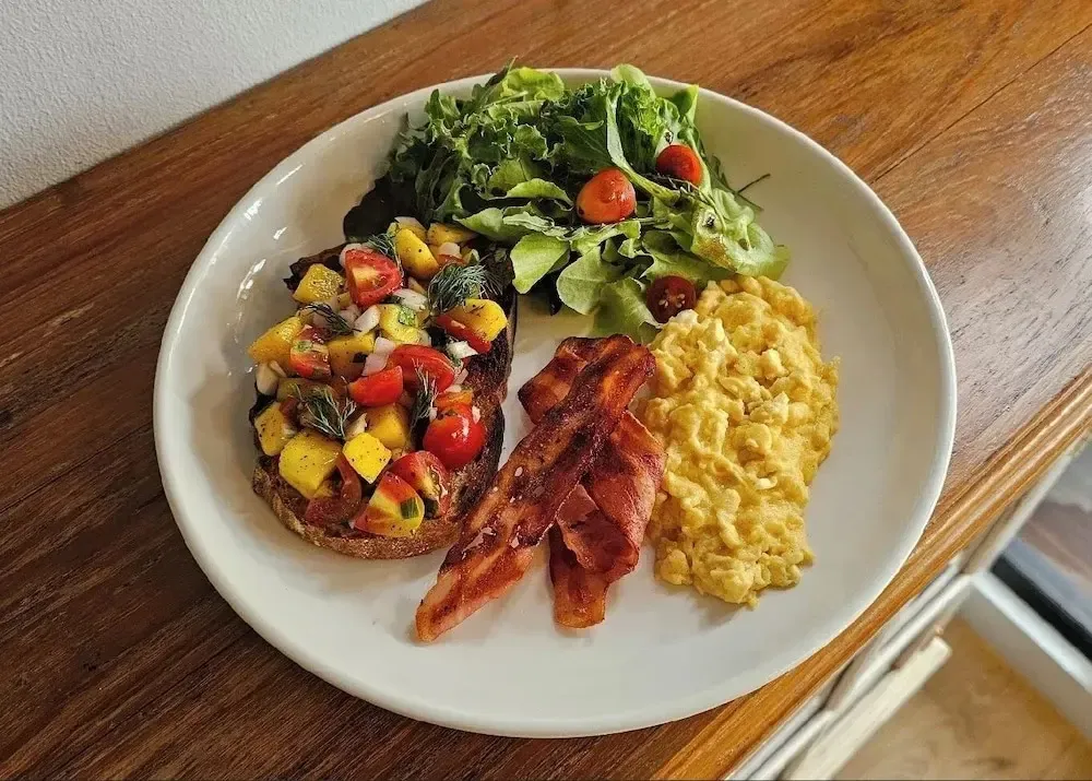 Assiette copieuse avec des œufs brouillés, du bacon, des tranches de pain garnies et une salade verte.