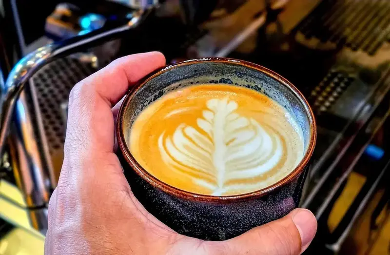Une main présente une tasse de café au lait décorée d'un motif en latte art.