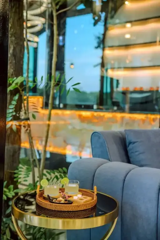 Une table basse avec des boissons est placée devant un canapé bleu dans un espace lumineux.