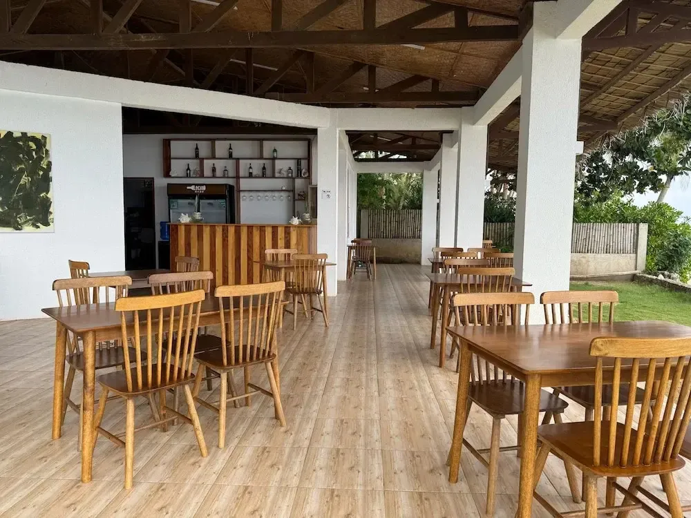 Une salle à manger extérieure avec des tables en bois et un bar en fond.