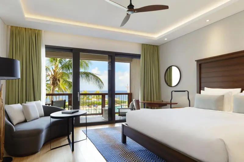 Une chambre lumineuse avec un lit et un coin salon donnant sur une vue sur la mer.