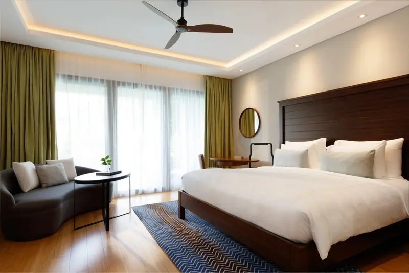 Une chambre lumineuse avec un grand lit et un coin salon près de la fenêtre.
