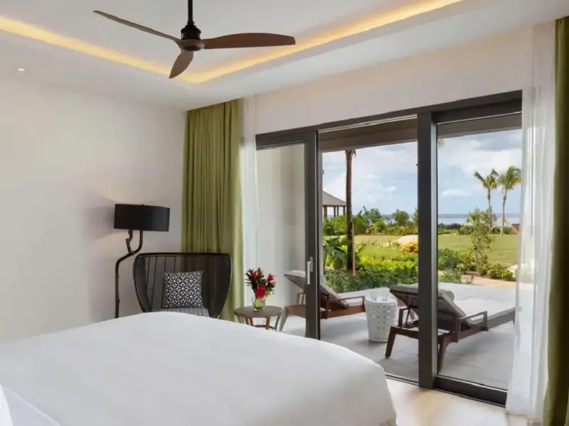 Une chambre lumineuse s'ouvre sur une terrasse avec vue sur un jardin tropical.