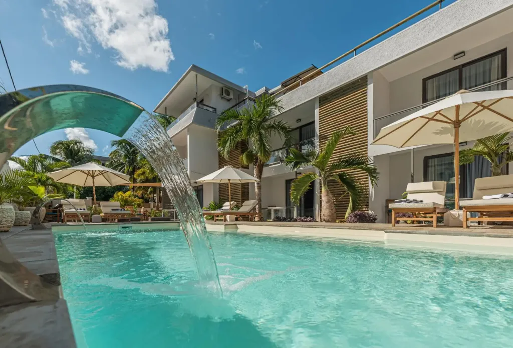 Une cascade d'eau se déverse dans une piscine turquoise bordée de transats et de parasols.
