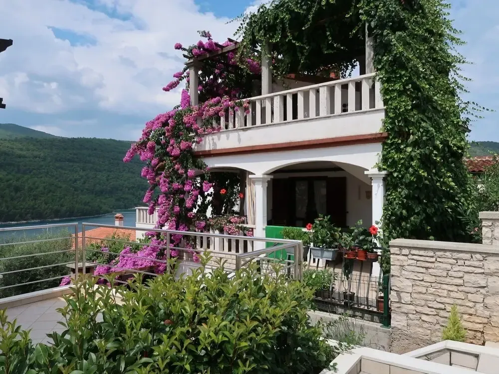 Bâtiment blanc orné de fleurs grimpantes avec balcon et vue sur la mer.