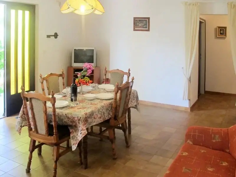 Une table à manger est mise avec de la vaisselle et une bouteille de vin dans une pièce lumineuse.