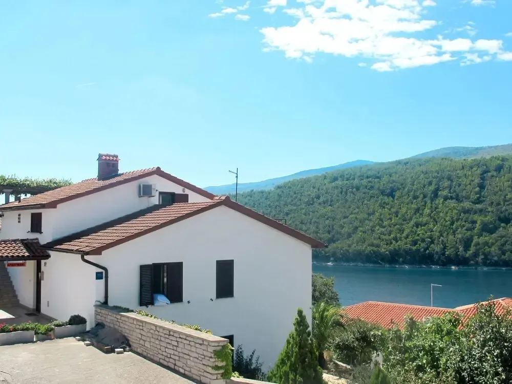 Bâtiment blanc avec toit en tuiles rouges surplombant un paysage verdoyant et une étendue d'eau.