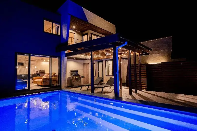 Une piscine illuminée devant une maison moderne avec une terrasse couverte.