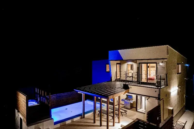 Bâtiment moderne éclairé la nuit avec piscine et terrasse couverte.