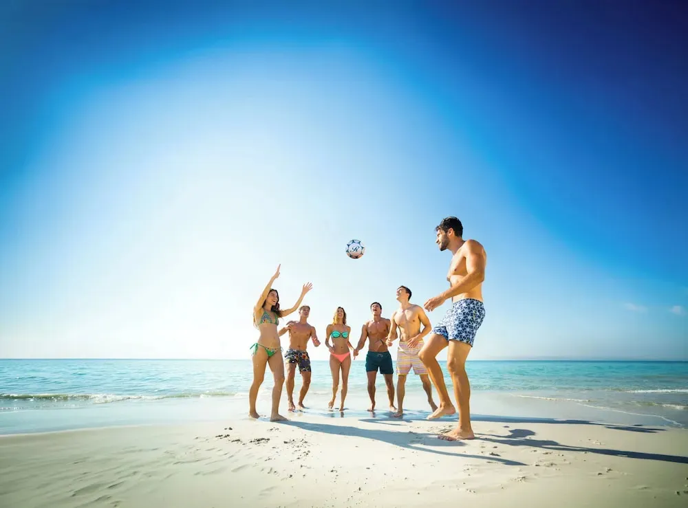Un groupe de personnes joue avec un ballon sur une plage de sable blanc.