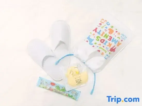 Un ensemble de chaussons, d'articles de toilette et d'un jouet pour enfants est présenté sur une surface claire.