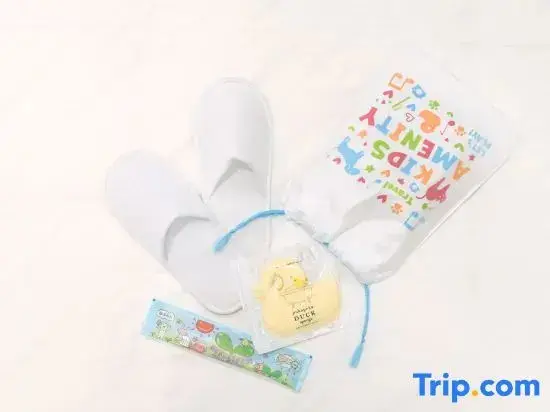 Un ensemble de chaussons, d'articles de toilette et d'un jouet pour enfants est présenté sur une surface claire.