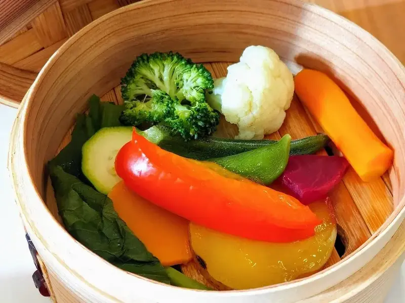 Assortiment de légumes colorés cuits à la vapeur dans un panier en bambou.
