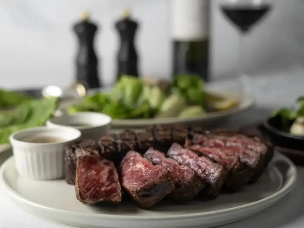 Une portion de viande tranchée est servie avec une salade et une sauce.
