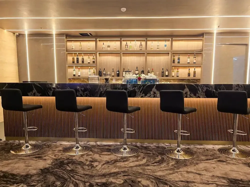 Un comptoir de bar moderne avec des tabourets hauts et une étagère remplie de bouteilles.