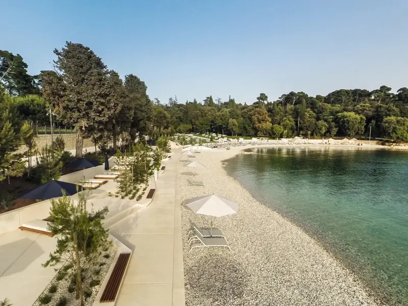 Vue aérienne d'une plage de galets bordée de parasols et de transats.