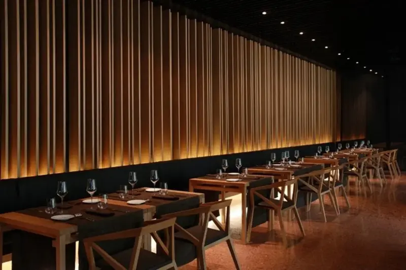 Une salle de restaurant élégante avec des tables dressées et un mur décoratif en bois éclairé.
