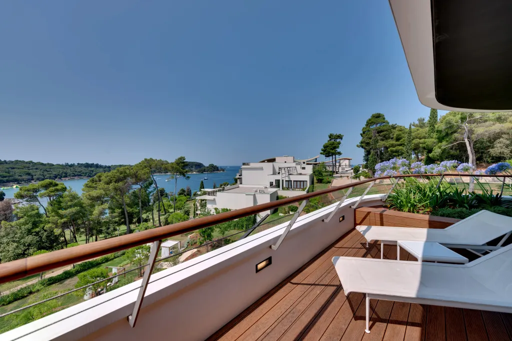 Terrasse en bois avec transats donnant sur une vue mer et des bâtiments.