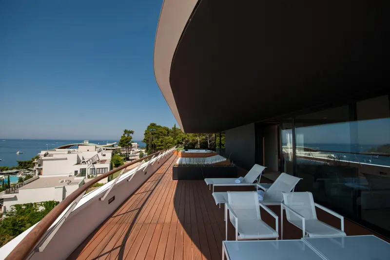 Terrasse en bois avec chaises longues donnant sur la mer et les bâtiments environnants.