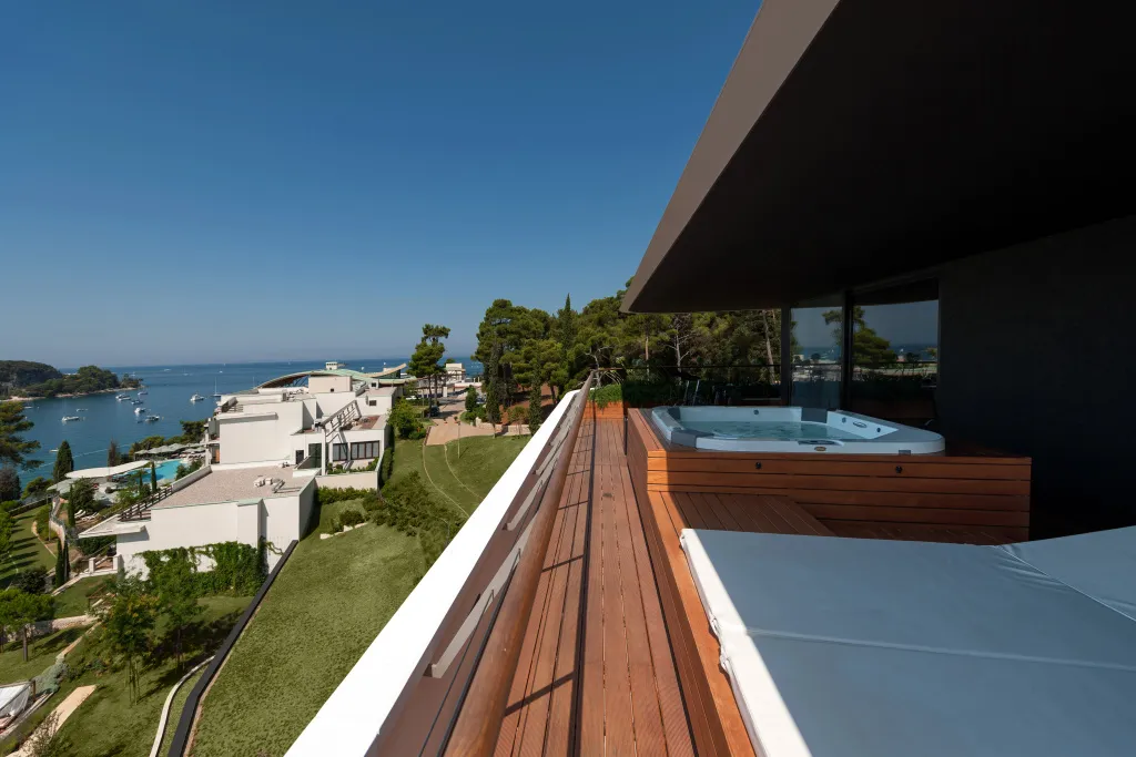 Terrasse en bois avec jacuzzi et vue sur la mer et les bâtiments environnants.