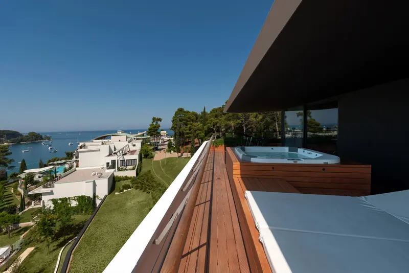 Terrasse en bois avec jacuzzi et vue sur la mer et les bâtiments environnants.