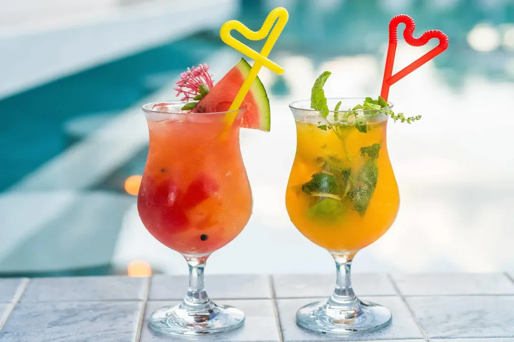 Deux cocktails colorés sont présentés sur une table près d'une piscine.