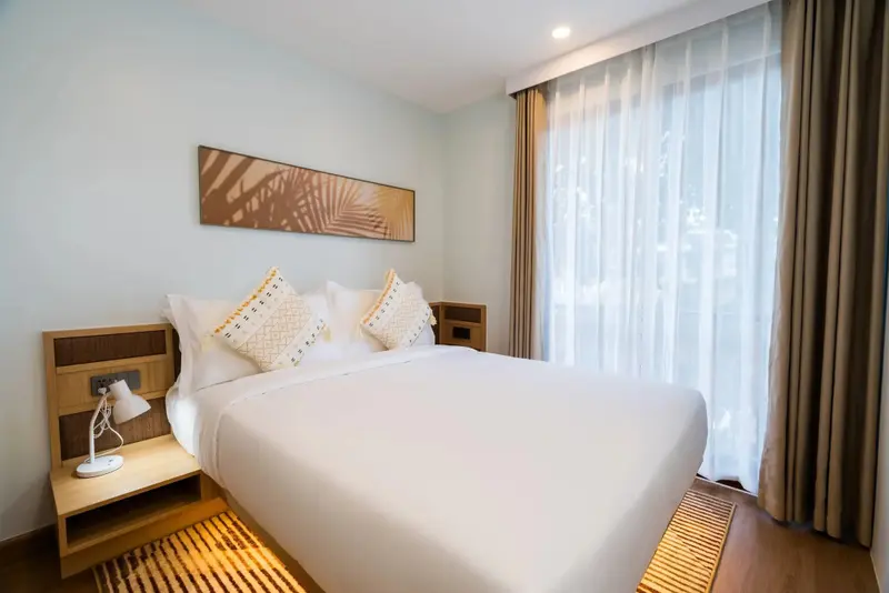 Une chambre lumineuse avec un grand lit recouvert d'une courtepointe blanche et de coussins décoratifs.