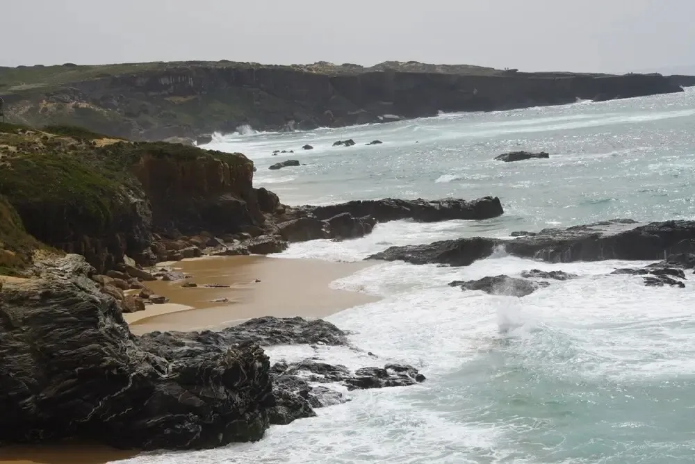 Une plage de sable fin bordée de rochers et de vagues.