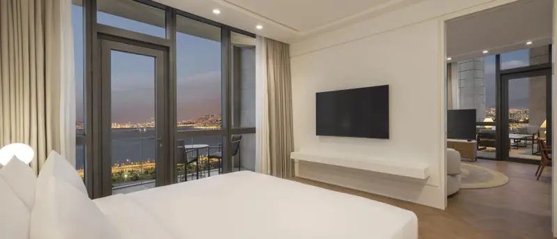 Une chambre lumineuse avec un grand lit face à une baie vitrée donnant sur une vue nocturne.