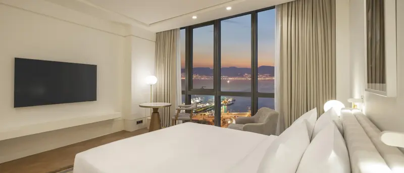 Une chambre lumineuse avec un grand lit et une vue sur la mer au coucher du soleil.