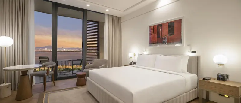 Une chambre lumineuse avec un grand lit et un accès à un balcon offrant une vue sur la mer.