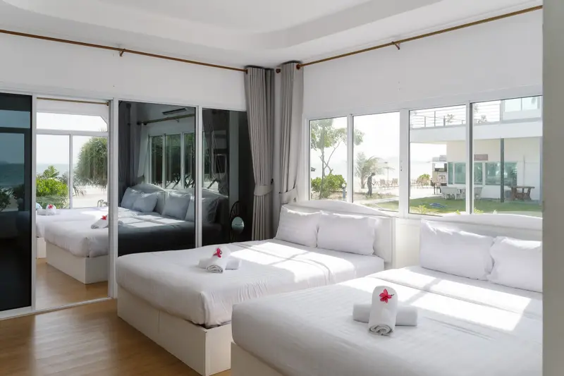 Chambre lumineuse avec lits soignés et vue sur un jardin tropical.