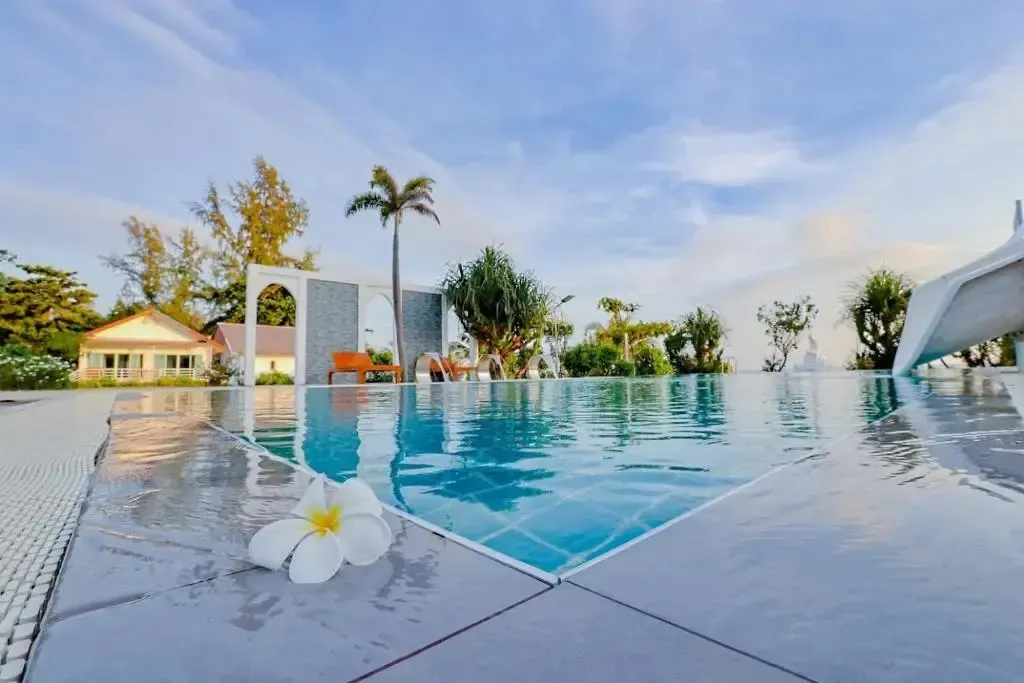 Une piscine rectangulaire au bord d'une plage avec des transats et des palmiers.