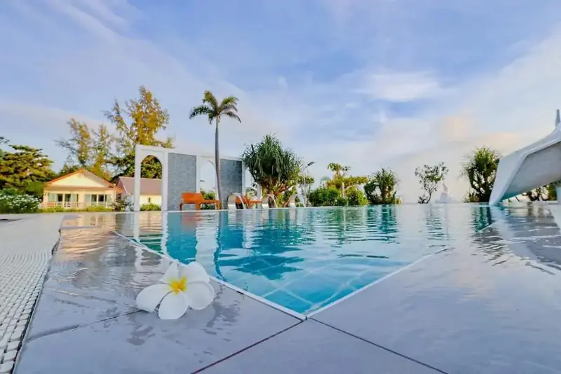 Une piscine rectangulaire au bord d'une plage avec des transats et des palmiers.