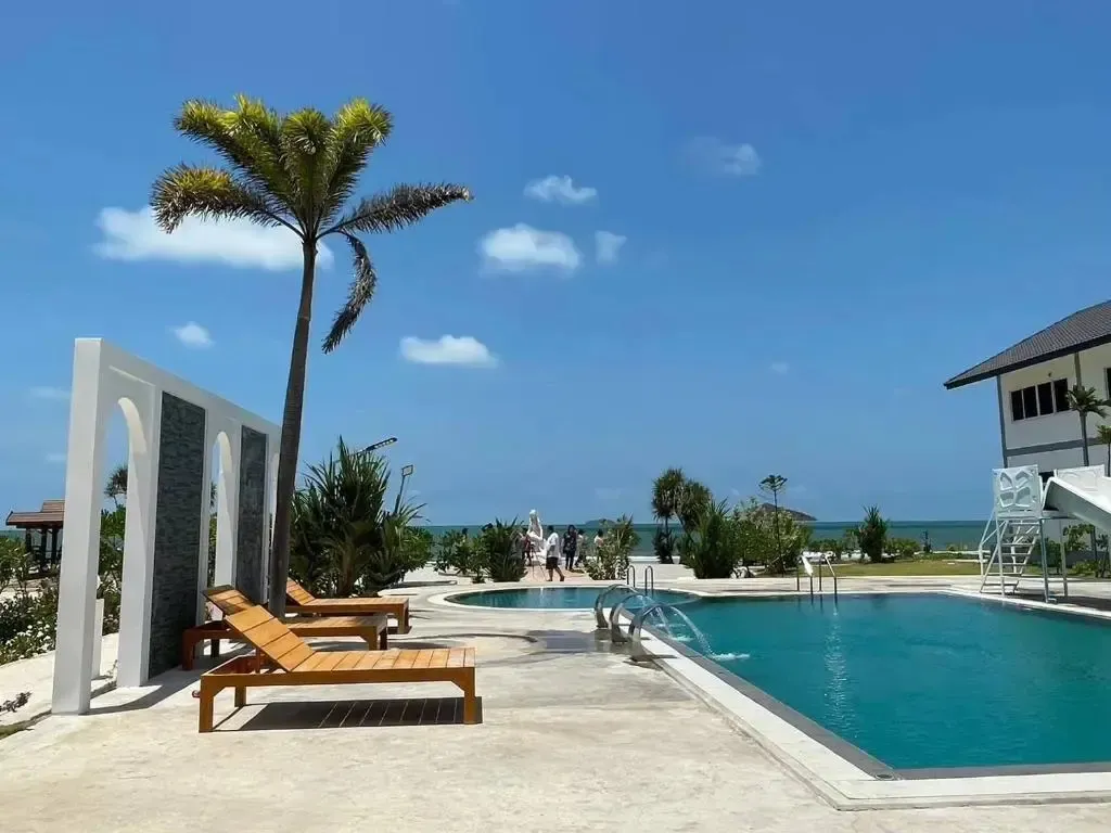 Transats et piscine en bord de mer sous un ciel bleu nuageux.