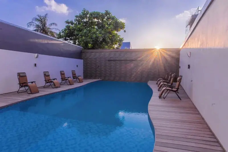 Une piscine rectangulaire bordée de chaises longues et de végétation.