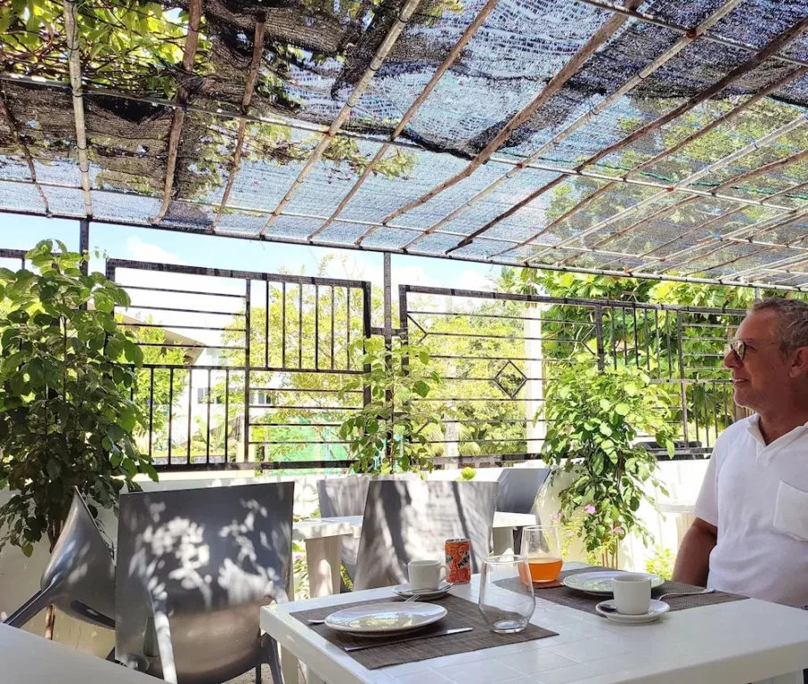 Une personne est assise à une table en extérieur, sous une structure ombragée.