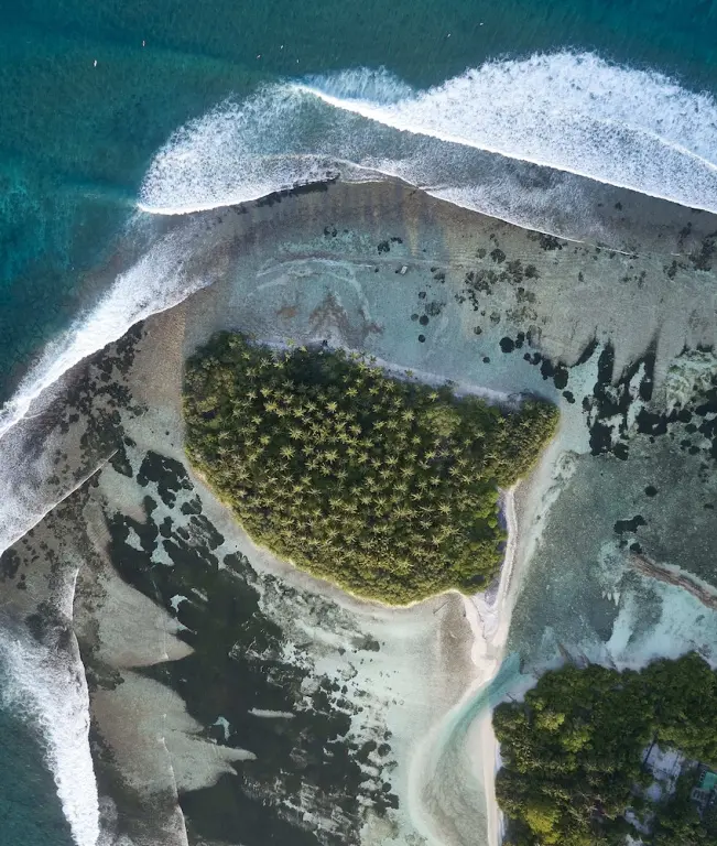 Vue aérienne d'une île tropicale entourée de plages et de vagues.